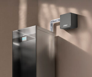 Industrial metal electrical cabinet with a small touchscreen display connected to a wall-mounted power junction box via conduit.